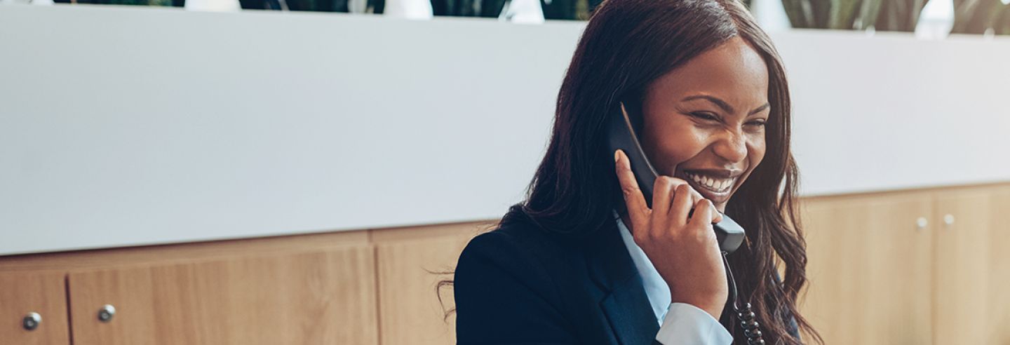 Vrouw zit lachend aan bureau met telefoon aan haar oor