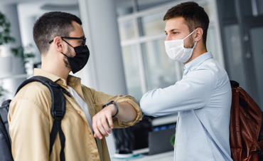 Twee mannen met mondmasker geven elkaar ellebooggroet